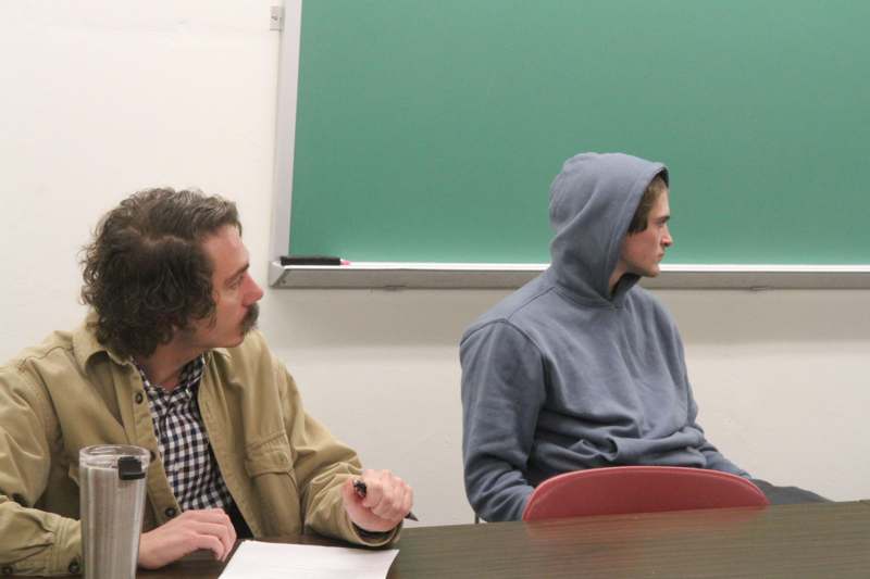 a man sitting at a desk with a man in a hoodie