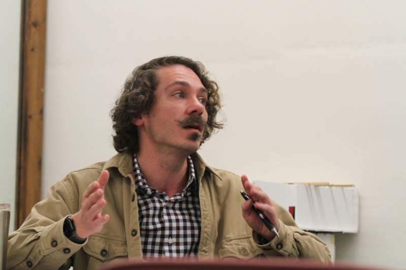a man with curly hair and mustache holding a pen