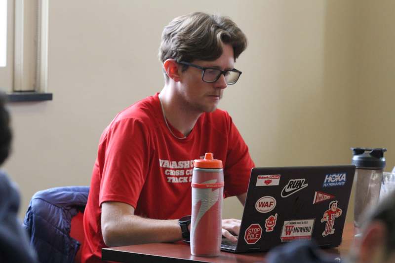 a man in a red shirt sitting at a table with a laptop
