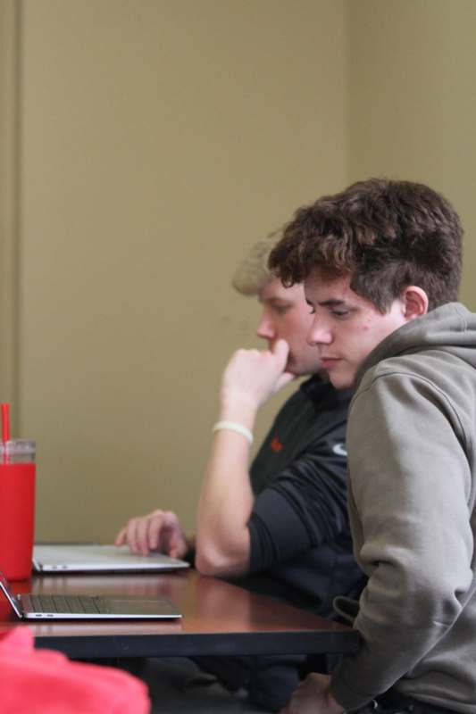 two men sitting at a table looking at a laptop