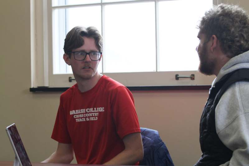 a man in glasses talking to another man