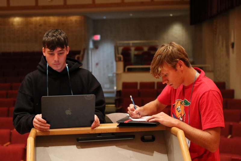 a couple of men sitting at a table with a laptop and a notepad