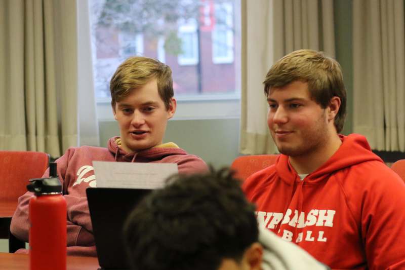 a group of men sitting at a table looking at a laptop