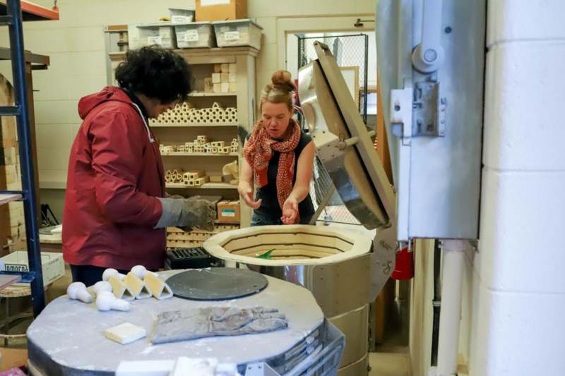 a woman standing next to a woman in a room with a large round object
