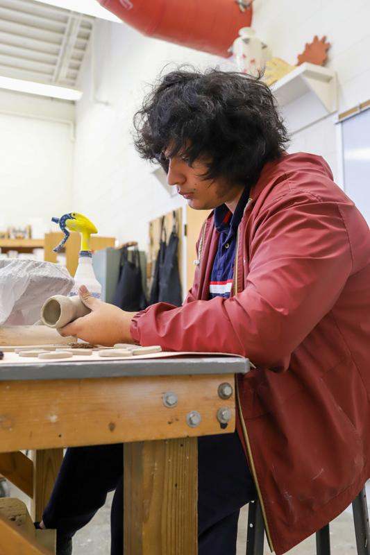 a man in a red jacket working on a clay piece