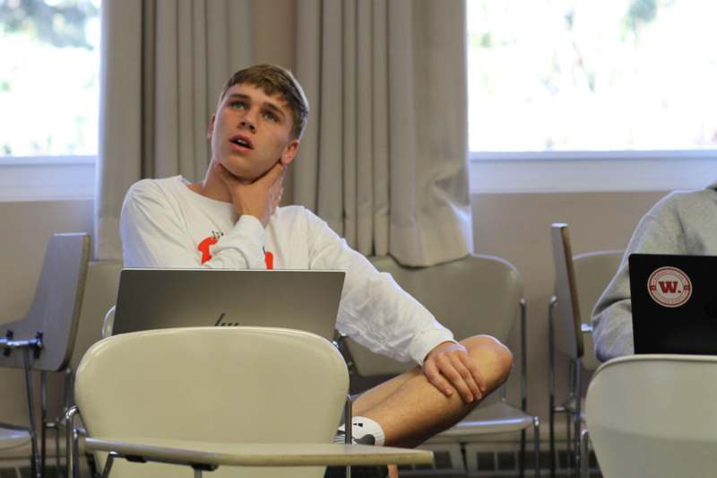a man sitting in a classroom with his hand on his neck