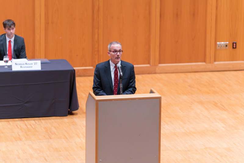 a man in a suit and tie speaking at a podium