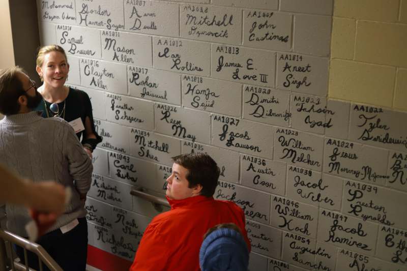 a group of people standing in front of a wall with names