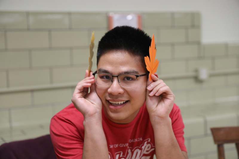 a man wearing glasses and holding up paper leaves on his ears
