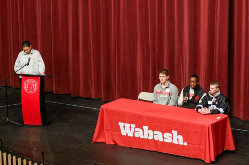 a man standing at a podium with a red table with a red tablecloth and a man standing at a podium