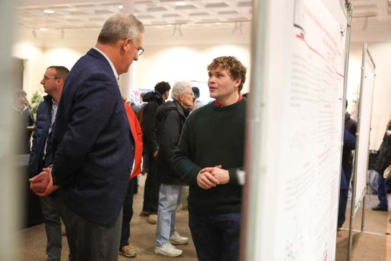 a man talking to a man in a room with people