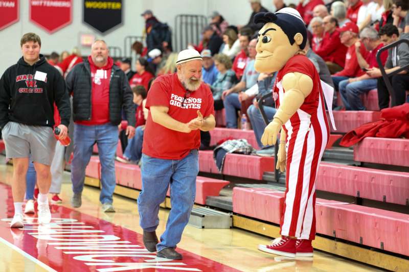 a man in a red shirt and white hat with a mascot in front of a crowd