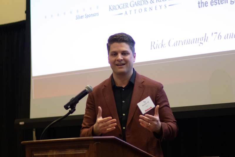 a man standing at a podium with a microphone and a small white card