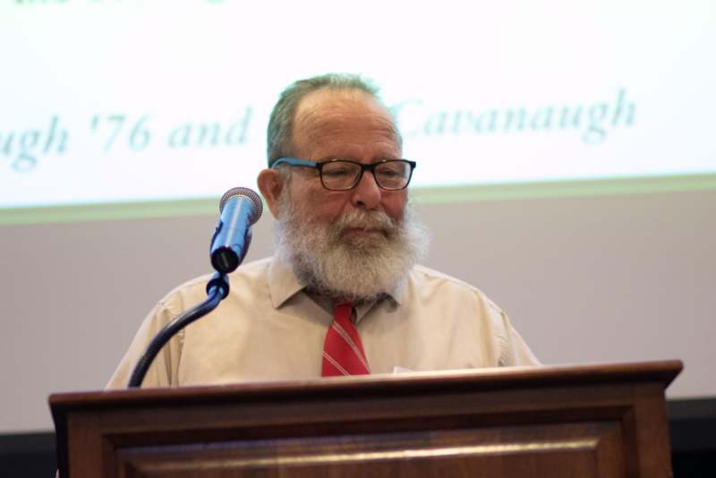a man with a beard and glasses standing at a podium with a microphone