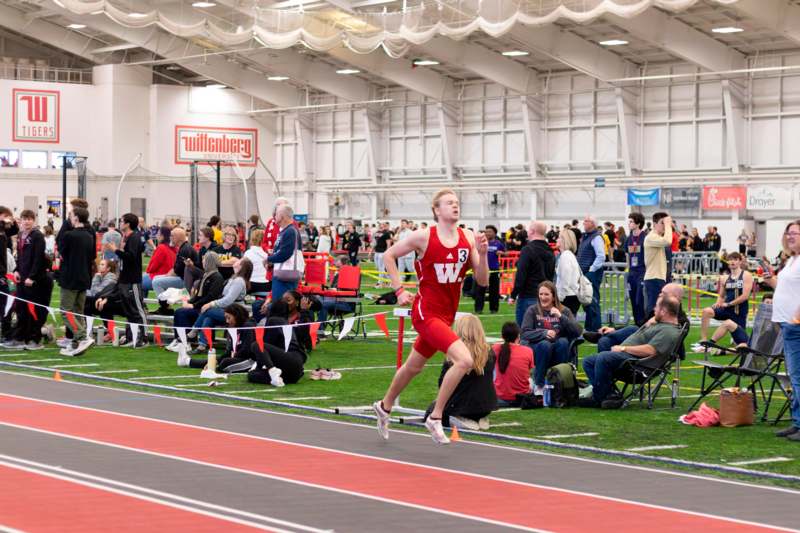 a man running on a track in a large building with people watching