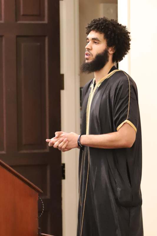 a man with a beard standing in front of a wooden staircase