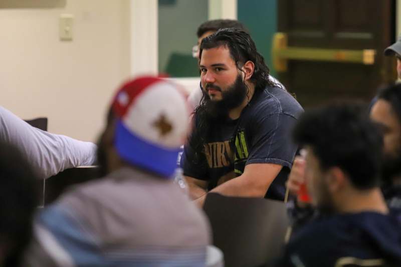 a man with long hair sitting in a room with other people