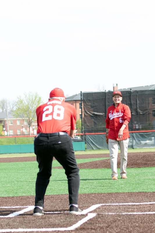 a man in red shirt and black pants standing on a field with a baseball glove