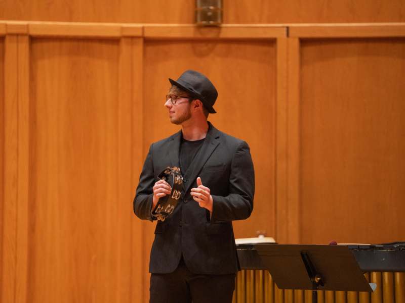 a man in a black suit and hat holding a tambourine