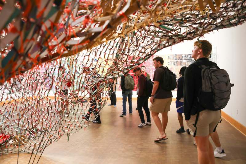 a group of people standing in a room with a large piece of art