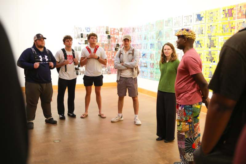 a group of people standing in a room with a wall of pictures