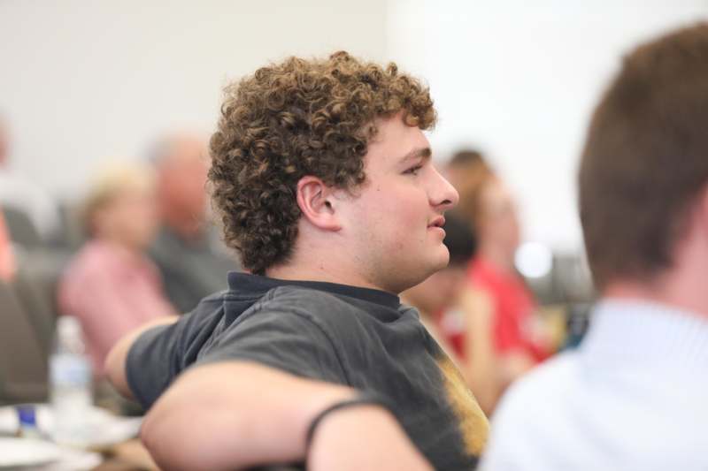 a man with curly hair sitting in a room with other people
