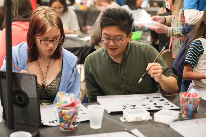 a man and woman sitting at a table with a computer and a paper
