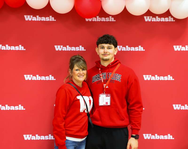 a man and woman standing in front of a red wall with balloons