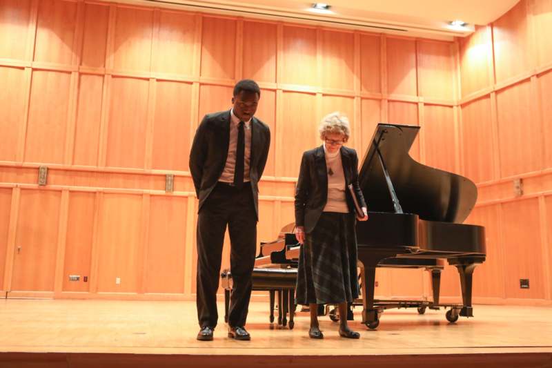 a man and woman standing on a stage with a piano