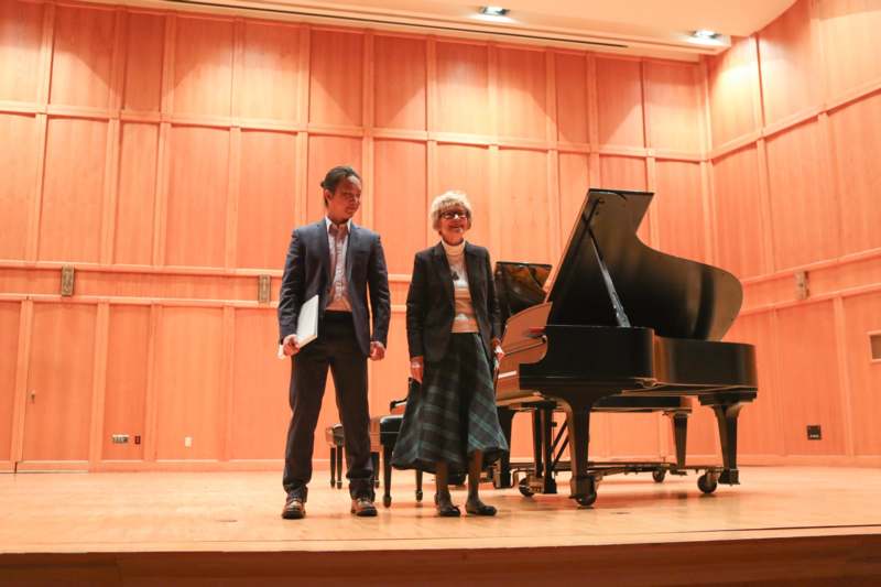 a man and woman standing on a stage with a piano