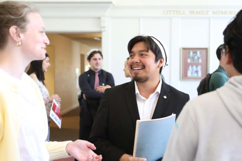 a man in a black suit and white headband holding a blue book