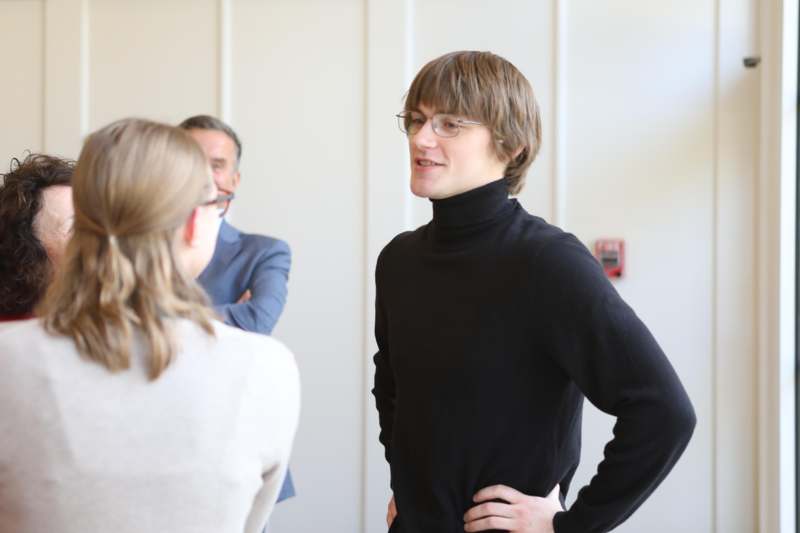 a man in a black turtleneck and glasses talking to a woman