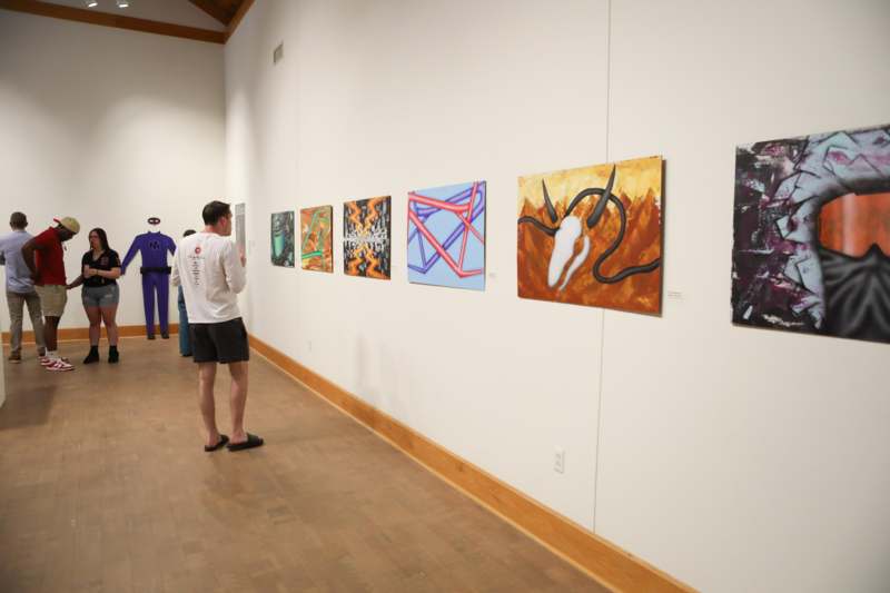 a man looking at a wall with paintings on it
