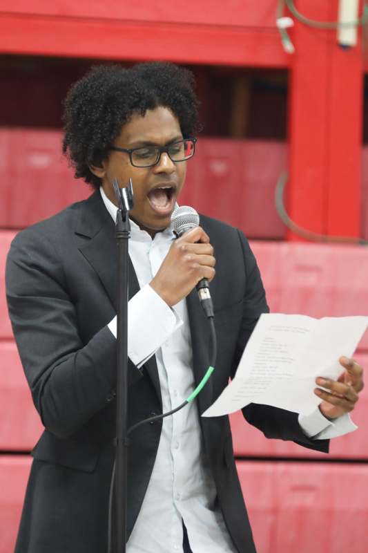 a man in a suit holding a microphone and reading a paper