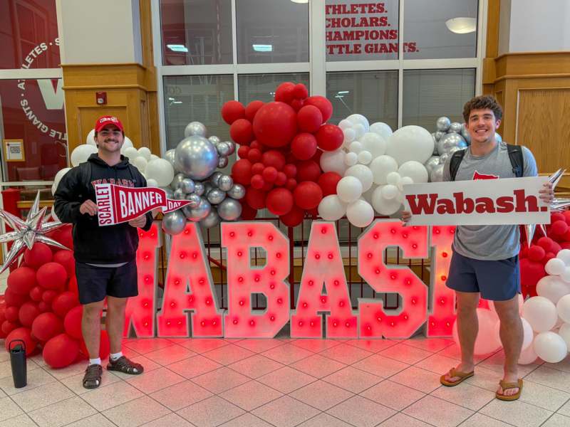 two men standing in front of a large sign with balloons