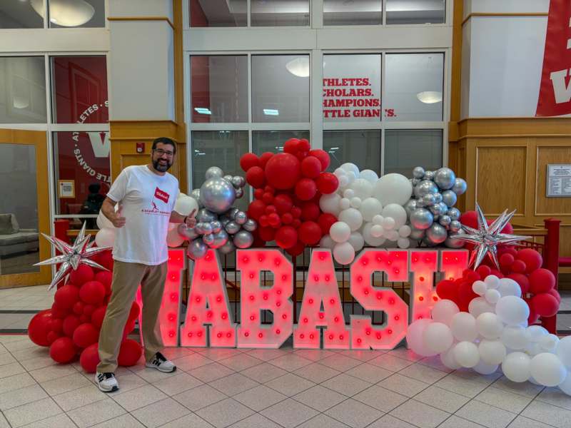 a man standing in front of a large sign with balloons