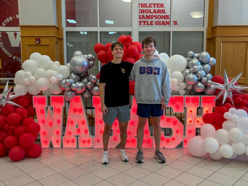 two men standing in front of a large sign with balloons
