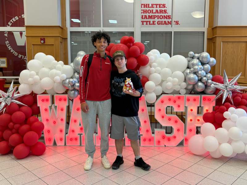 two men standing in front of a large sign with balloons
