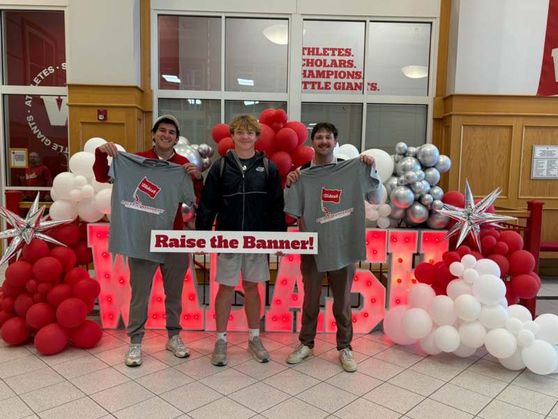 a group of men posing for a photo with balloons and a sign