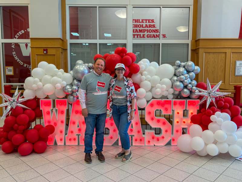 a man and woman standing in front of a large sign with balloons