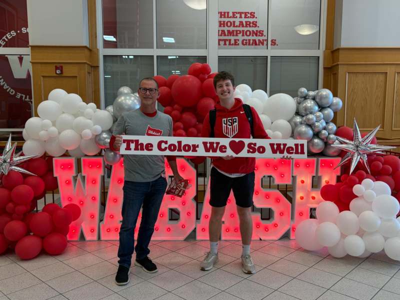 two men posing for a photo with balloons and a sign
