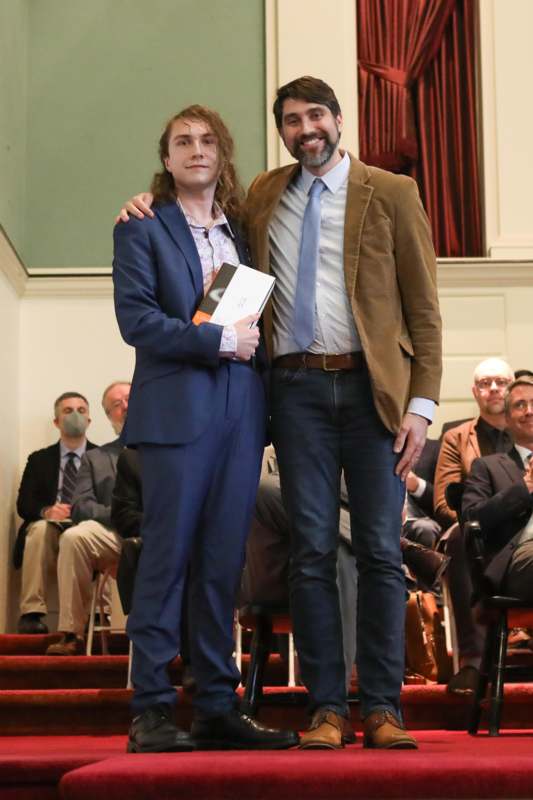 two men standing together in front of a crowd of people