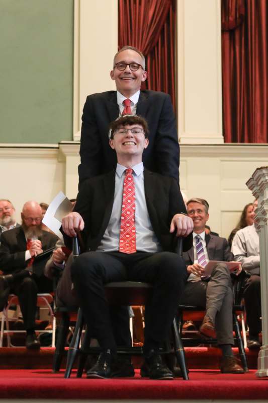 a man sitting on a chair with another man on his shoulders