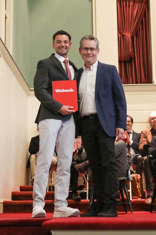 two men standing on stairs with a red book