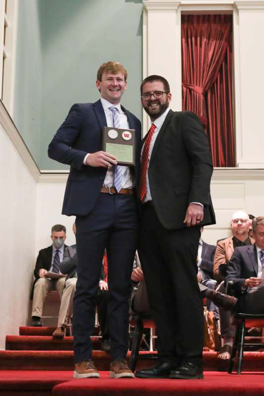 two men standing on stairs holding a plaque