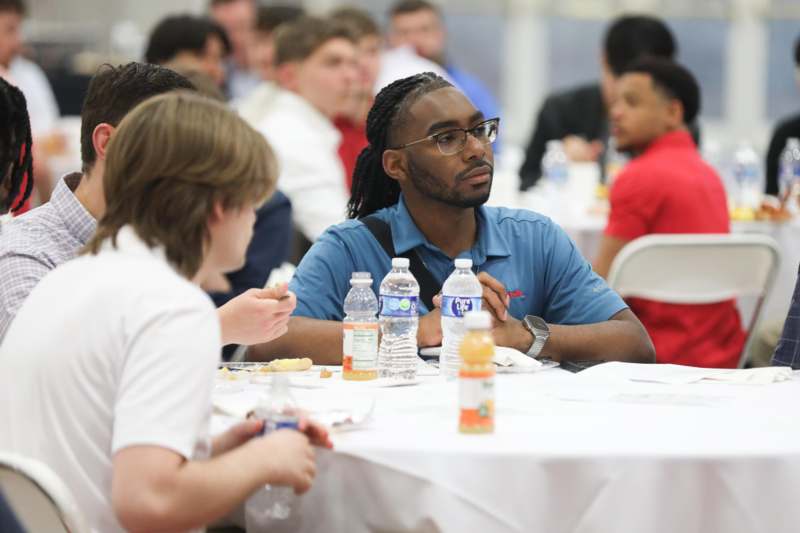 a man sitting at a table with water bottles and a group of people