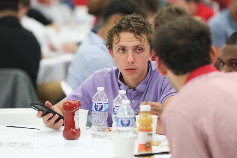 a man sitting at a table with a phone and bottles of ketchup