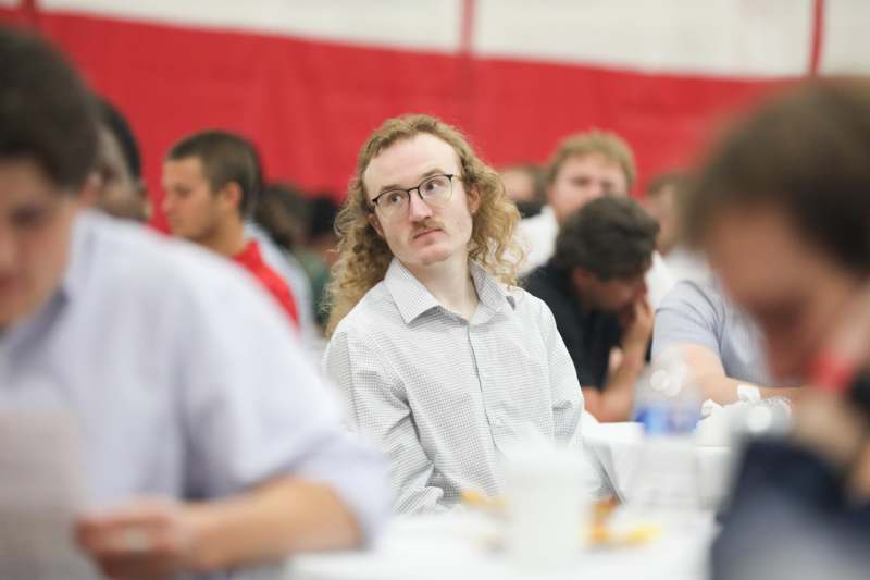 a man with long hair sitting at a table with other people