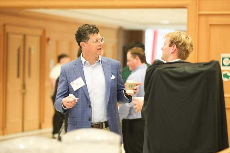 a man in a suit holding a cup and talking to another man