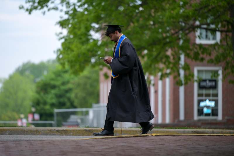 a man in a graduation gown and cap walking down a sidewalk